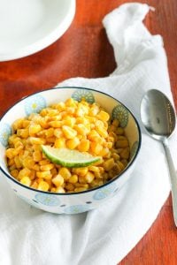 Mexican Corn topped with lime Wedge in white bowl.