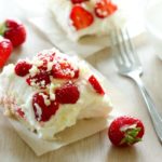Strawberry shortcake square topped with whipping cream and sliced strawberries.