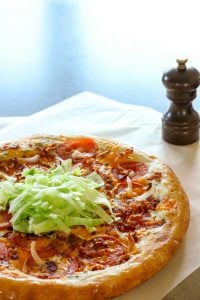 Pizza topped with tomatoes and shredded lettuce on parchment paper.