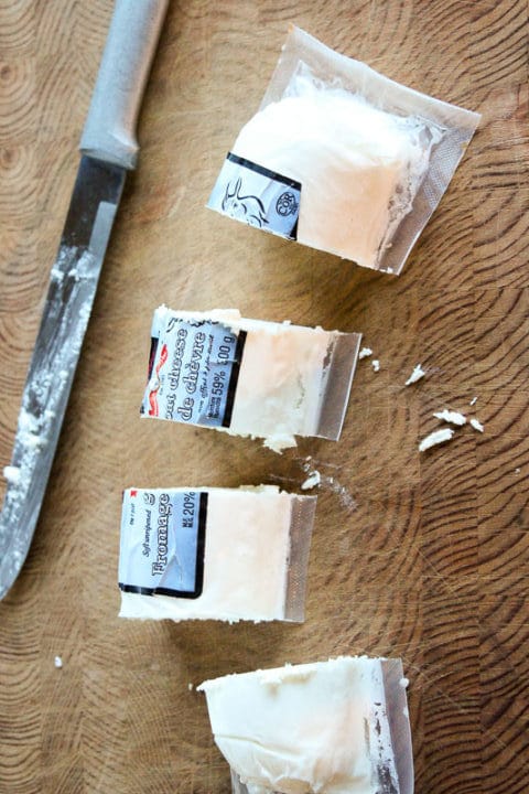 Sliced package of goat cheese on wooden board.