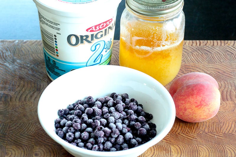 Frozen Blueberries, Yogurt, Honey and a Peach on Wooden Board.