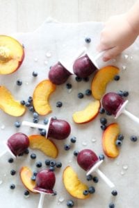 Child reaching for blueberry popsicle next to sliced peaches.