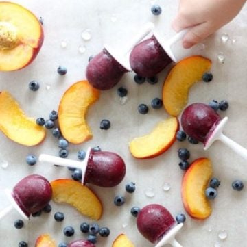 Child reaching for blueberry popsicle next to sliced peaches.