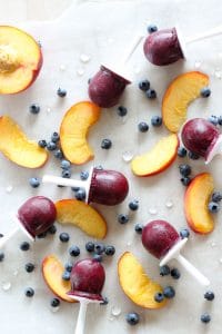 Blueberry peach posicles on wax paper with sliced peaches and blueberries