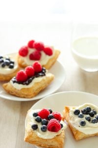 5 pastries topped with icing and fruit on white plates.