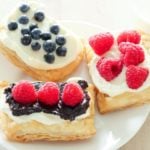 Three pastries topped with icing and berries on white plate.