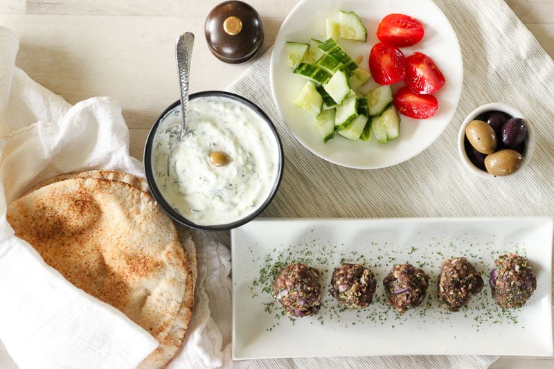 Greek Meatballs on White Rectangular Plate with Vegetables, Bread and Tzatziki.