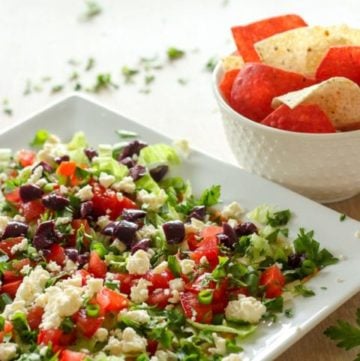 Healthy dip with feta, black olives and other vegetables on white plate.