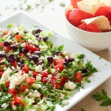 Healthy dip with feta, black olives and other vegetables on white plate.