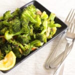Roasted broccoli in black dish with lemon slice.