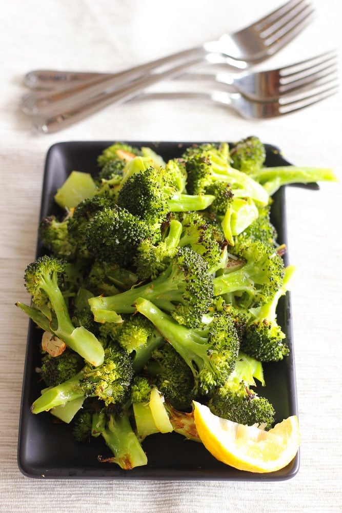 Oven Roasted Broccoli and Lemon Wedge on Black Plate.