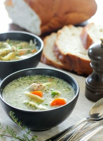 Two black bowls of creamy chicken soup and loaf of bread