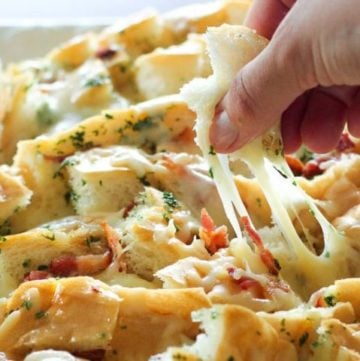 Hand pulling apart cheesy bacon bread.