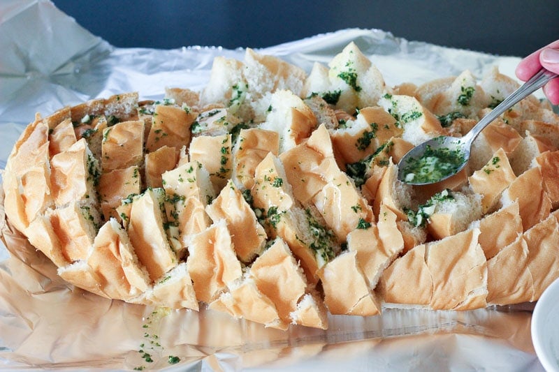 Pouring Butter, Garlic and Parsley Mixture on Sliced Loaf of Bread.