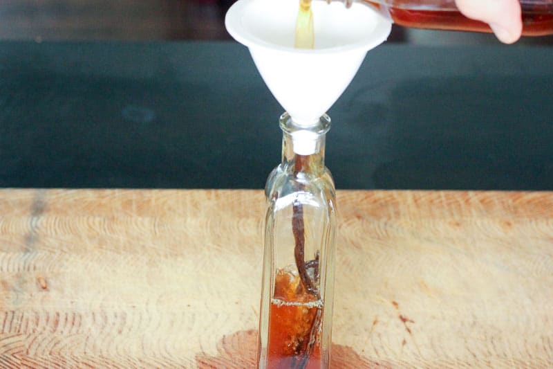 Pouring Vanilla Extract into White Funnel into Narrow Glass Bottle.