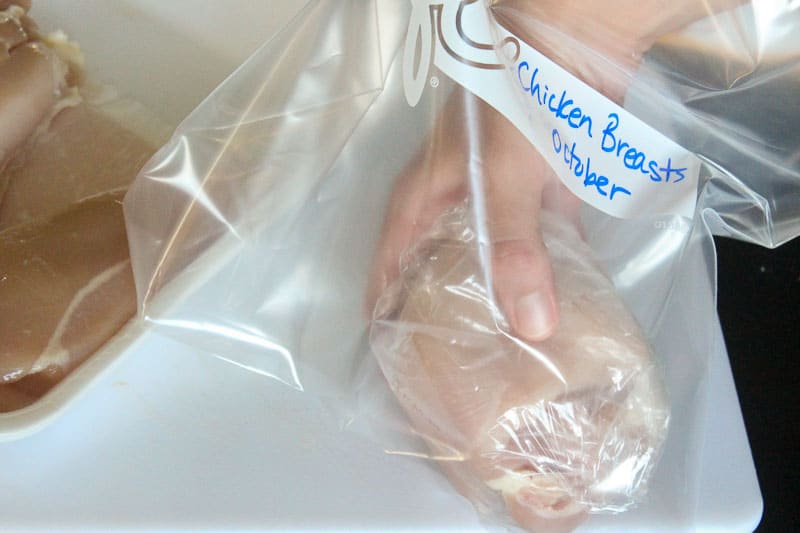 Hand putting raw chicken in large resealable bag.
