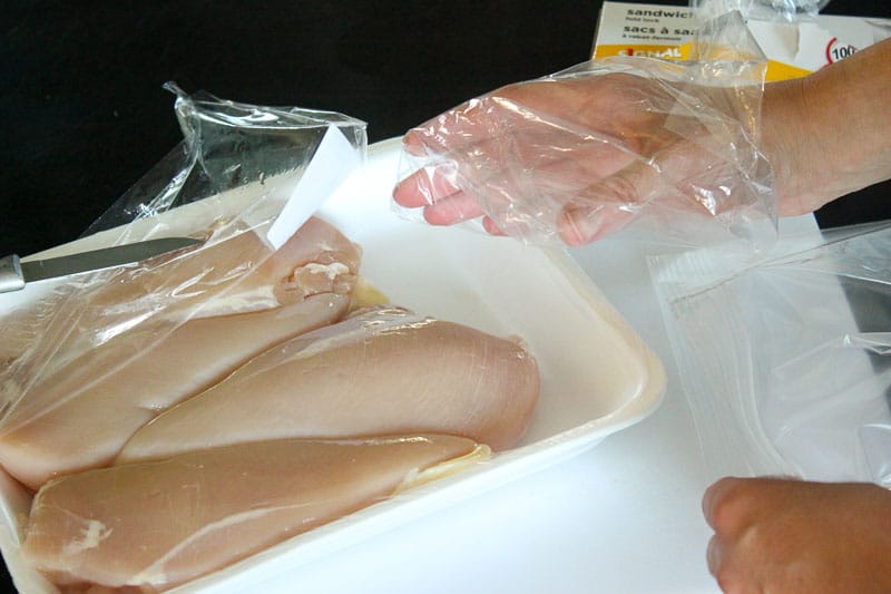 Hand in resealable plastic bag picking up raw chicken Breast.