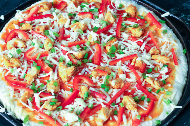 Thai Barbecue Chicken Pizza Topped with Shredded Mozzarella Cheese on Round Pizza Pan.