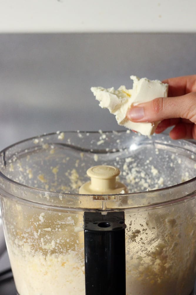 Adding cream cheese to garlic and feta in food processor.