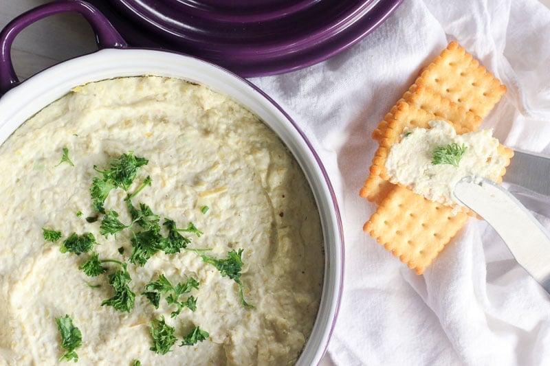 Whipped Artichoke and Feta Dip topped with Parsley in a baking dish, served with crackers.