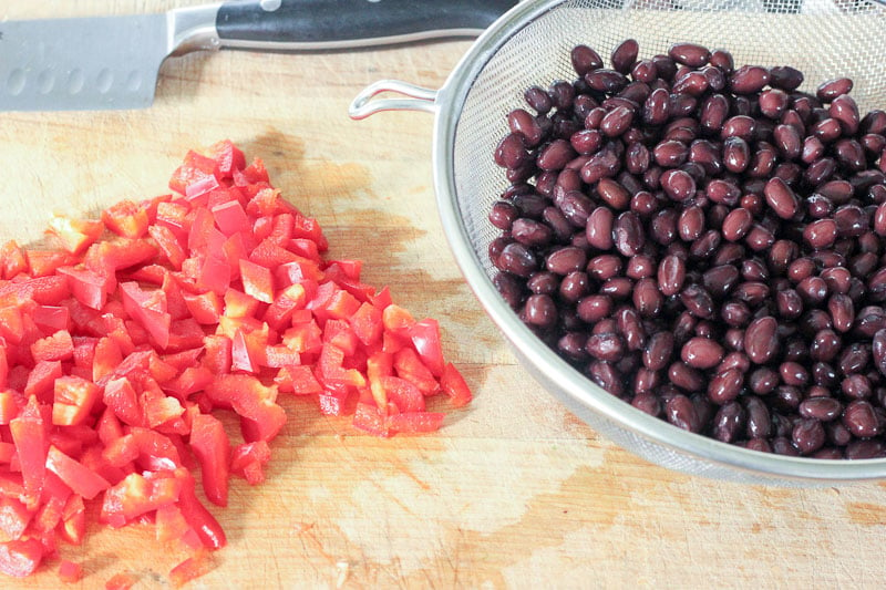 Chopped Red Peppers on Wooden Board and Black Beans in Metal Colander.