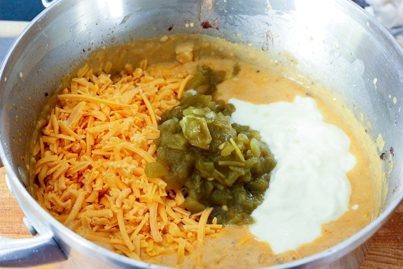 Adding Shredded Cheddar Cheese, Chopped Green Chillies and Yogurt to Metal Pot.