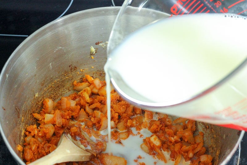 Pouring Milk into Fried Onions and Spices in Metal Pot.