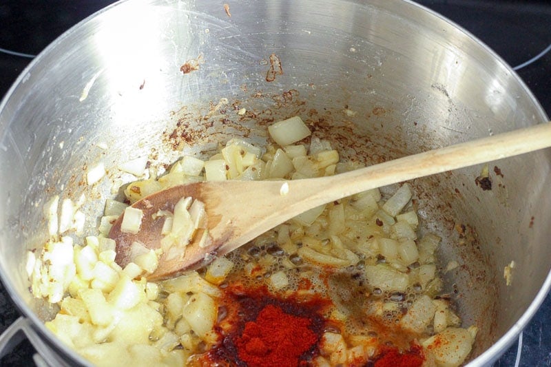 Adding Spiced to Frying Onions in Metal Pot.