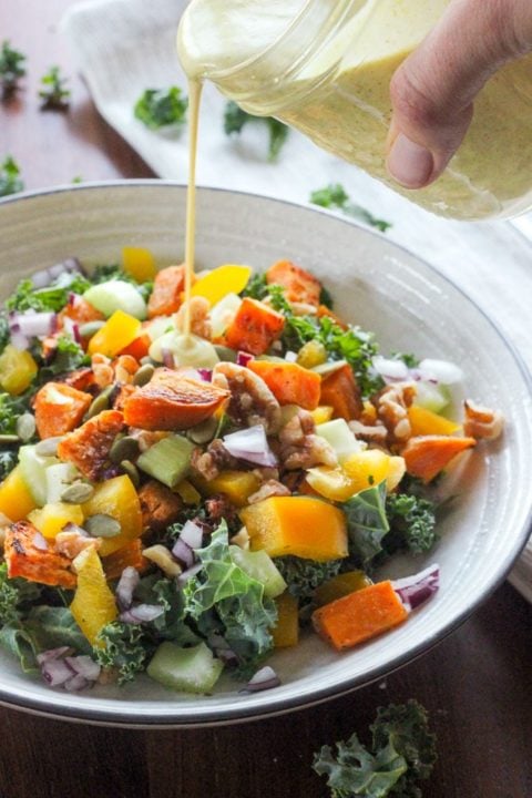 Healthy salad with kale, sweet potato and other vegetables in white bowl.