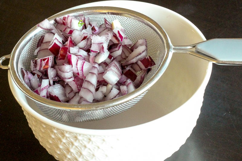 Draining Water from Chopped Red Onion over White Bowl.