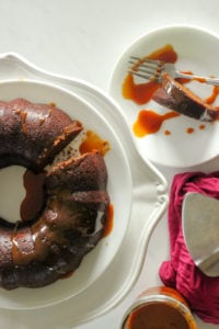Gingerbread cake topped with caramel sauce on white plate.