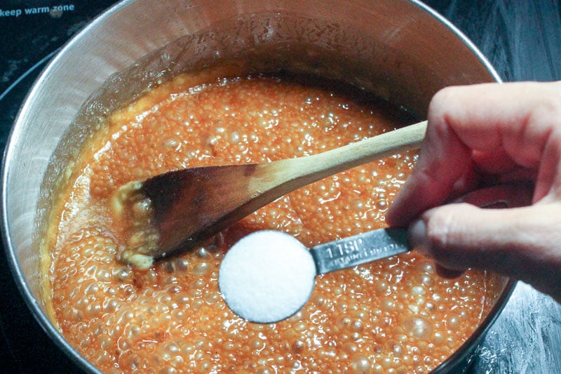 Adding Salt to Boiling Caramel Sauce in Metal Pot.