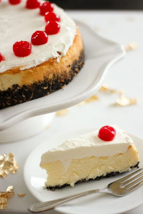 Slice of cheesecake topped with cherry on white plate.