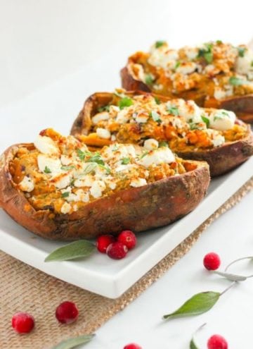 Halved sweet potatoes topped with goat cheese and herbs on white plate.