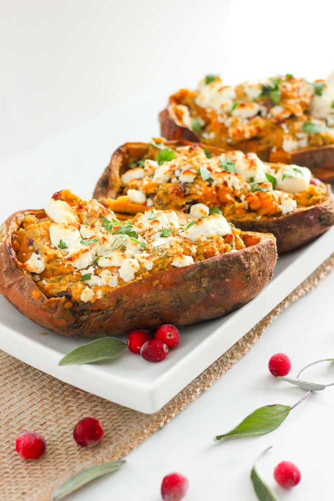 Healthy Twice Baked Sweet Potatoes Topped with goat cheese, cranberries and herbs on White Plate.