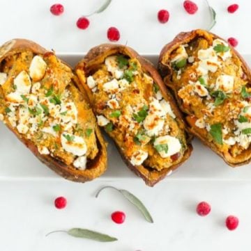 3 halved sweet potatoes topped with goat cheese and herbs on white plate.