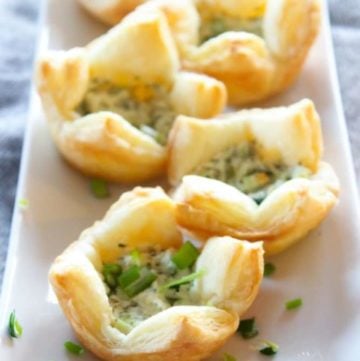 Puff pastries filled with goat cheese and herbs on white plate.