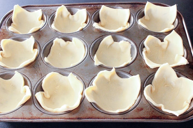 Gently press puff pastry squares into muffin tin for Herb and Goat Cheese Puff Pastry Bites - An Easy Party Appetizer!