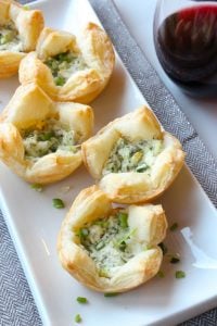 Puff pastry bites filled with herbs and cheese on white plate.