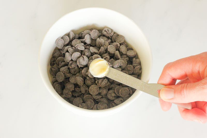 Adding Butter to White Bowl of Chocolate Chips.