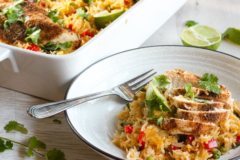 One Pan THAI Chicken and Rice Bake topped with Cilantro and Lime Wedge in White Plate.