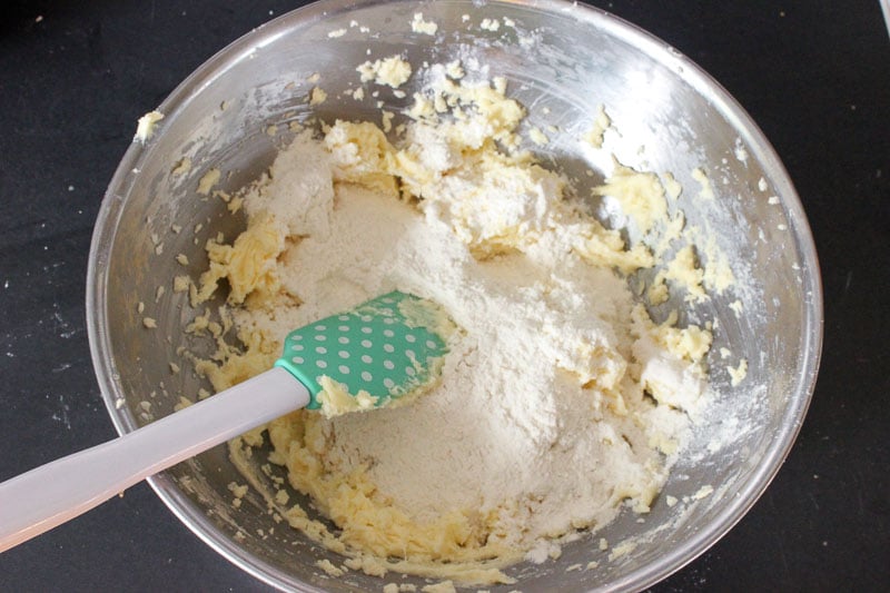 Adding dry ingredients to butter, vanilla and Sugar Mixture in Metal Mixing Bowl.