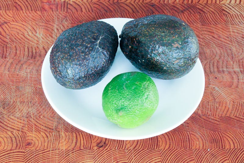 Two Avocados and One Lime on Small White Plate.