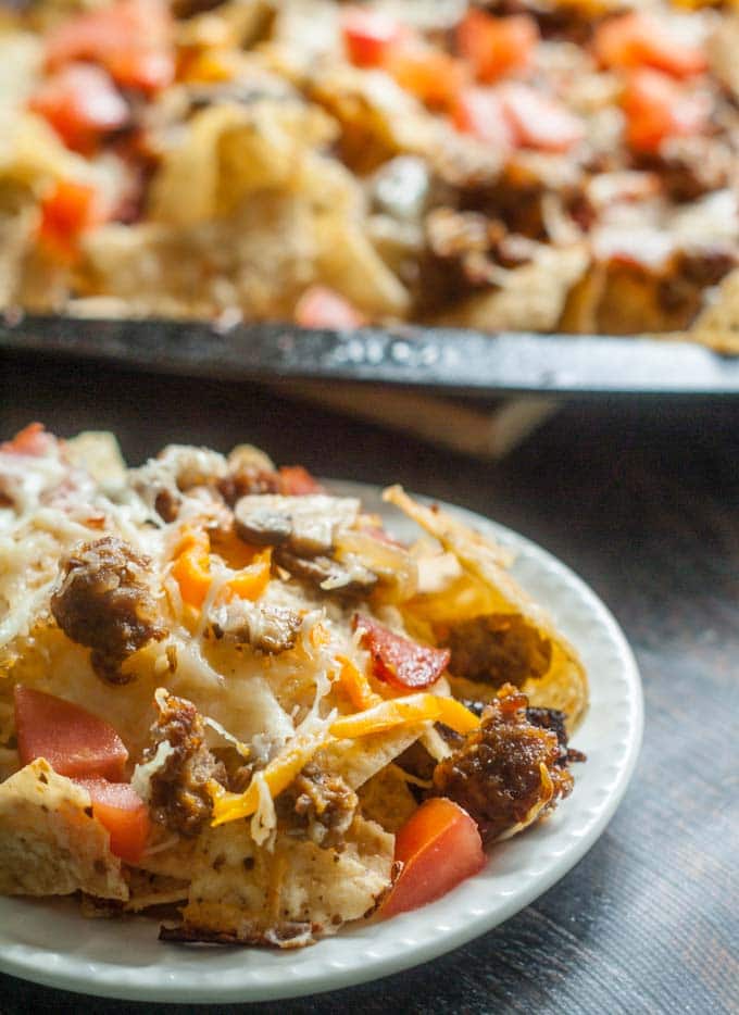 Nacho Chips topped with Sausage, Tomatoes and Cheese on White Plate.