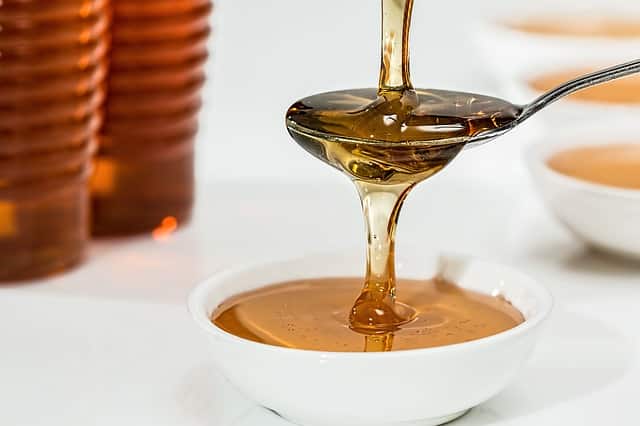Honey pouring into spoon and overflowing into bowl.