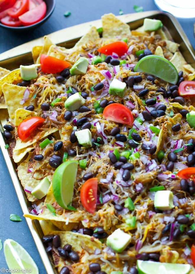 Nacho Chips in Sheet Pan topped with Tomatoes, Avocado, Black Beans and Lime Wedges.