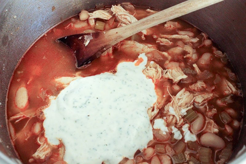 Adding Ranch Dressing to Buffalo Chicken Chili in Metal Pot.