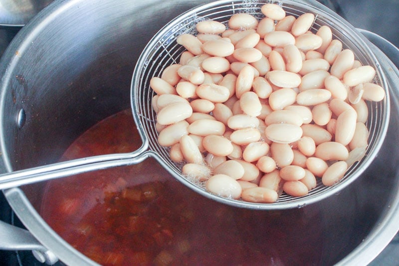 White Beans in Metal Sieve above pot of soup.