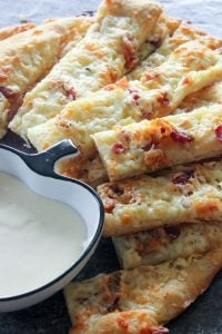 Stacked Garlic Fingers topped with Bacon next to bowl of Donair Sauce.