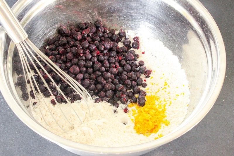 Frozen blueberries, lemon zest and dry muffin ingredients in a bowl.